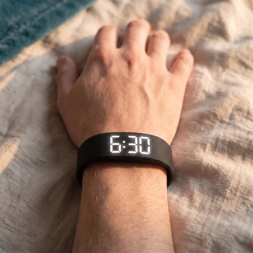 The Touchwake band worn like a watch, display reading 6:30, on a hand resting on linen sheets